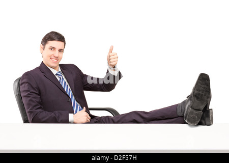 Junge lächelnde Unternehmer sitzen auf einem Stuhl mit seinen Beinen und einen Daumen aufgeben isoliert auf weißem Hintergrund Stockfoto