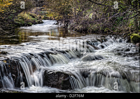 River bei Crosthwaite gehen über ein Wehr mit alten Brücke im Hintergrund Stockfoto