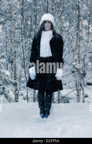 eine Frau in einem schwarzen Mantel mit einem weißen Hut und weißen Schal im Schnee Stockfoto