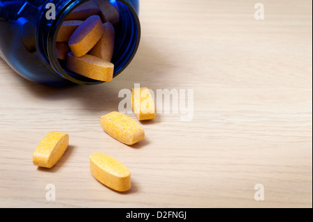 Blaue Flasche gelb Vitaminpillen mit einigen Verschütten auf den Tisch Stockfoto