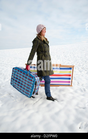 Winterurlaub bedeckt Urlauber zu Fuß über Schnee, Feld tragen Koffer & Liegestuhl Stockfoto