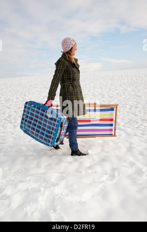 Winterurlaub bedeckt Urlauber zu Fuß über Schnee, Feld tragen Koffer & Liegestuhl Stockfoto