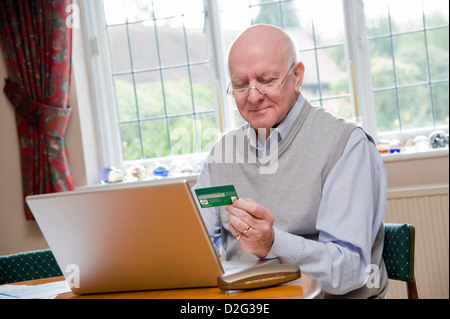 Ältere Mann mit Laptop, um Rechnungen zu bezahlen / online-shopping mit Kreditkarte Stockfoto