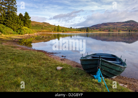 Reflexion an der entfernten Loch Ordie, nr Dunkeld, Schottland, aufgenommen kurz nach Sonnenaufgang mit türkisfarbenen Ruderboot im Vordergrund Stockfoto