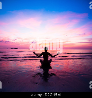 Junge Frau praktizieren Yoga am Strand bei Sonnenuntergang. Stockfoto
