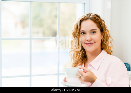 Lächelnde entspannte kaukasischen Frau von Fenster halten Tasse Kaffee Stockfoto