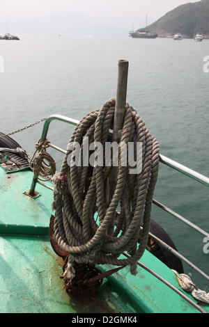 Es ist ein Foto von einem langen Seil, das um einen hölzernen Stock in einem Boot auf dem Meer aufrollt Stockfoto