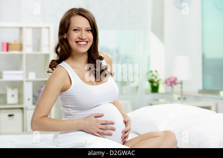 Foto ziemlich schwanger Frau halten Sie ihre Hände auf Bauch beim Blick in die Kamera Stockfoto