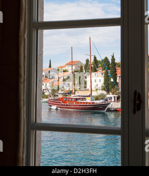 Blick aus einem Fenster mit Blick in eine Bucht mit einem traditionellen Gulet-Boot vertäut im Hafen bei der Ortschaft Maslinica, Solta. Stockfoto