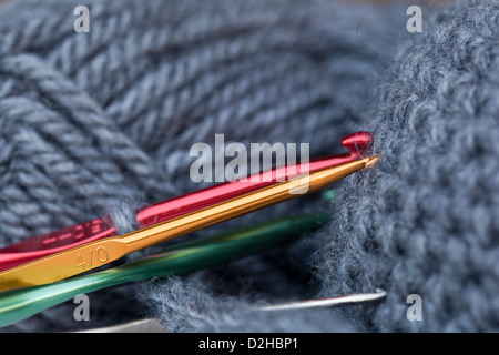 Nahaufnahme der bunten Häkelnadeln in einem grauen Garn. Stockfoto