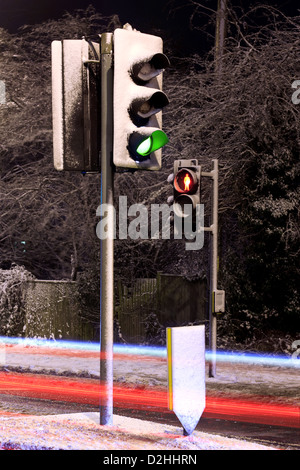 Ampeln bedeckt im Schnee auf einer UK-Straße in der Nacht mit Lichtspuren von vorbeifahrenden Autos. Stockfoto