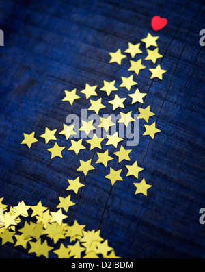 Glänzenden goldenen Sternen und rotes Herz in Form eines Weihnachtsbaumes auf einem dunkelblauen Hintergrund Holz Stockfoto