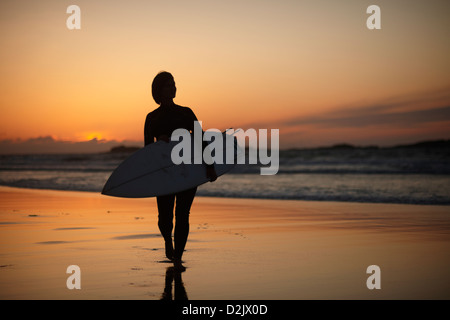 Surferin zu Fuß am Strand bei Sonnenuntergang / Sonnenaufgang Stockfoto