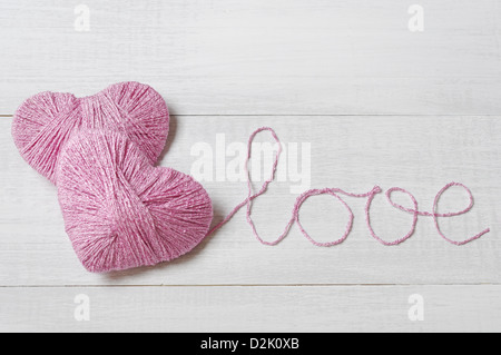 Zwei rosa Clews in Form von Herzen mit Wort 'Liebe' aus Garn auf weißem Hintergrund aus Holz gefertigt Stockfoto