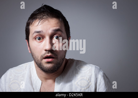 Young, bärtiger Mann mit erstaunten Gesichtsausdruck auf dunklem Hintergrund Stockfoto