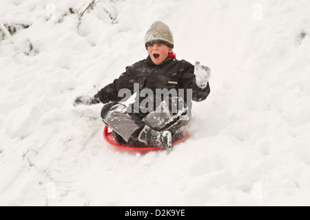 Junge geht auf Schlitten von einem Hügel im winter Stockfoto