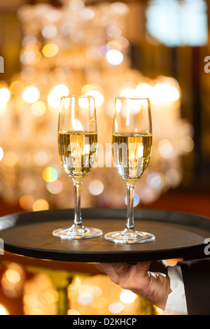 Kellner serviert Sektgläser auf einem Tablett in ein feines Restaurant, ein großer Kronleuchter im Hintergrund Stockfoto
