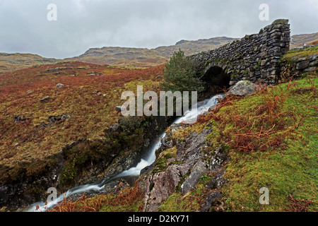 Ein Gebirgsbach unter der alten Steinbrücke über den Wrynose Pass in der Seenplatte, Cumbria, England Stockfoto