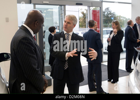 Ein weißer Geschäftsmann erklärt etwas mit einem schwarzen Geschäftsmann in einem belebten Raum. Stockfoto