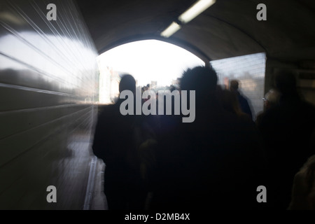 Verschwommene Menschen gehen in Richtung helles Sonnenlicht durch einen u-Bahn-Tunnel unter dem Damm im Zentrum von London. Stockfoto