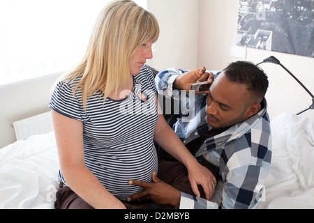 Weiße schwangere Frau mit schwarzen männlichen relaxen am Bett, während auf dem Handy zu sprechen Stockfoto