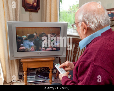 älterer Mann vor dem Fernseher zu Hause mittels TV-Fernbedienung Kanäle ändern Stockfoto