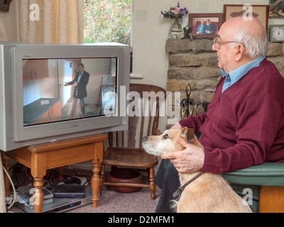 älterer Mann saß vor dem Fernseher mit seinem Hund an seiner Seite Stockfoto