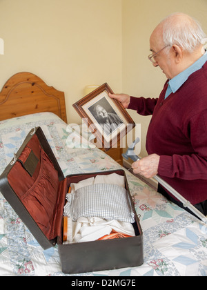 älterer Mann Foto des verstorbenen Frau Mutter im Schlafzimmer, während Verpackung, vielleicht zu verlassen oder Ankunft in ein Pflegeheim zu betrachten Stockfoto