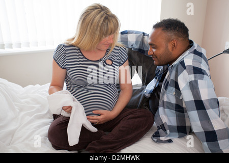 Schwangere weiße weibliche und schwarze männliche halten Baby-Kleidung Stockfoto
