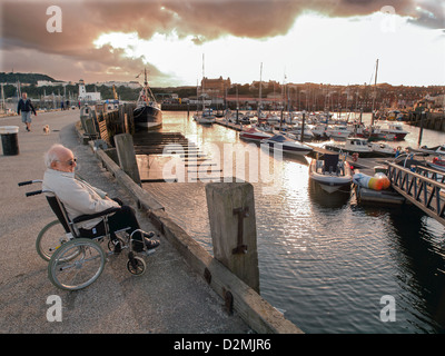 älterer Mann sitzt im Rollstuhl, Blick auf die Boote im Hafen Hafen Stockfoto