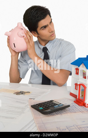 Real Estate Agent ein Sparschwein in der Nähe sein Ohr halten Stockfoto