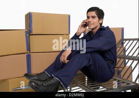 Speichern Sie Incharge sitzt auf einer Sackkarre und telefonieren mit einem Handy Stockfoto