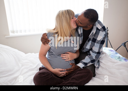 Schwangere weiße weibliche und schwarze männliche auf Bett Stockfoto