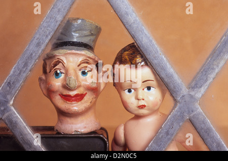 Misshandelte und gechipt papier Pappmaché männliche Marionette Kopf mit Hut neben junge Puppe mit mürrisches Gesicht Blick durch Fenster Stockfoto
