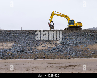 Eine mechanische Digger wird verwendet, um die Wartung und die Reparatur des Meer Abwehr auf dem Kiesel Ridge auf Westward Ho zu verpflichten! Strand. Devon, England. Stockfoto