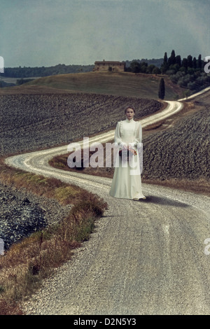 ein Mädchen in einem weißen Kleid geht entlang einer Gasse mit einem Korb voller Blumen in einer mediterranen Landschaft spazieren. Stockfoto