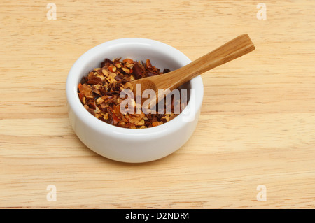 Chili-Flocken in ein Töpfchen mit einem Holzlöffel auf einem Holzbrett Stockfoto