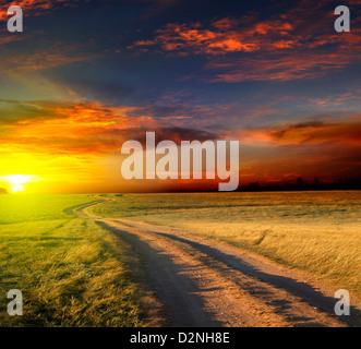 Landstraße durch ein Feld bei Sonnenuntergang Stockfoto