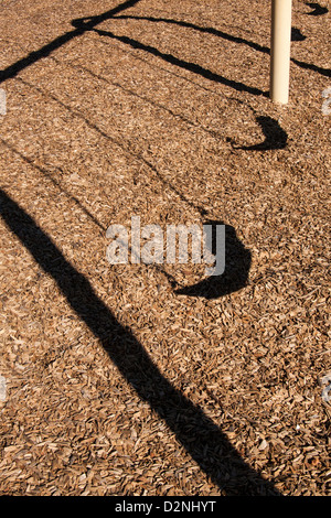 Auf ein Viertel-Spielplatz werfen Kinder Schaukeln lange Schatten auf die Rinde bedeckten Boden. Stockfoto