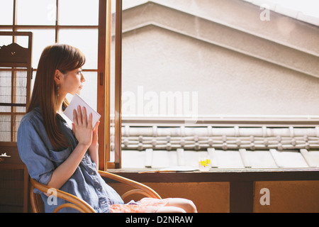 Junge Frau mit einem Buch aus dem Fenster schauen Stockfoto