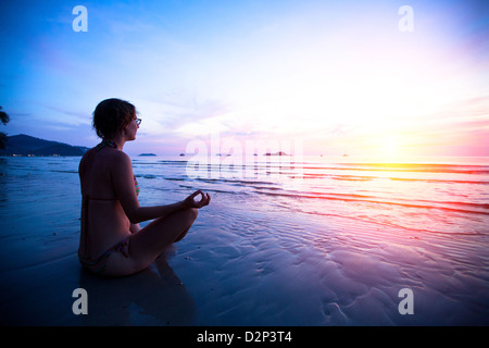 Junge Frau praktizieren Yoga am Strand bei Sonnenuntergang Stockfoto