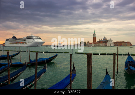 Riesige Kreuzfahrtschiff in der Lagune von Venedig in den frühen Morgenstunden mit Gondeln und San Giorgio Maggiore im Hintergrund. Urbino Stockfoto
