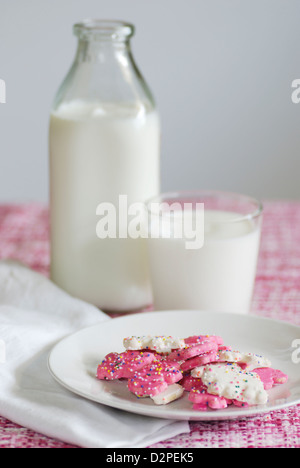 Rosa und weiß gefrostet Tier Cookies mit Streusel auf einem rosafarbenen und weißen Tweedstoff mit Flasche und Glas Kuhmilch Stockfoto