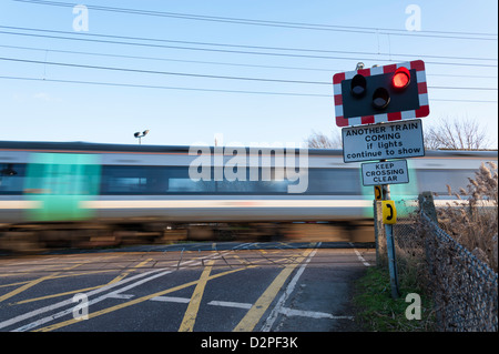 Ein Bahnübergang in einer ländlichen Gegend in Waterbeach Cambridge mit Warnleuchten blinken und Zug mit Geschwindigkeit geleitet Stockfoto