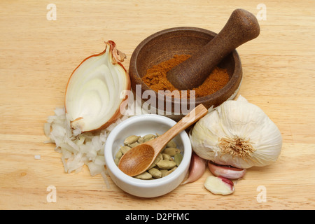 Curry-Zutaten, Zwiebel, Knoblauch, Kardamom und Curry-Pulver in einem Stößel und Mörser auf einem Holzbrett Stockfoto