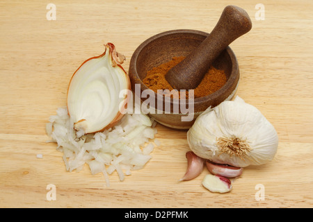 Zwiebel, Knoblauch und Currypulver in einem Stößel und Mörser auf einem Holzbrett Stockfoto