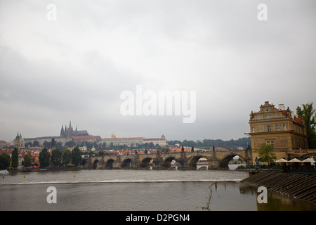 Panoramablick auf die Moldau mit Prager Burg und Karlsbrücke in der Ferne unter bewölktem Himmel Stockfoto