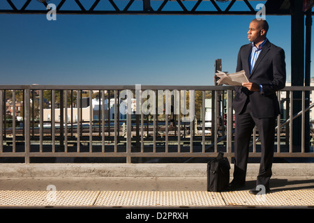 Schwarze Geschäftsmann, Zeitung lesen und warten am Bahnhof Stockfoto