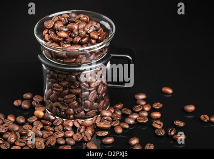 Becher mit ganzen gerösteten Kaffeebohnen auf schwarz Stockfoto