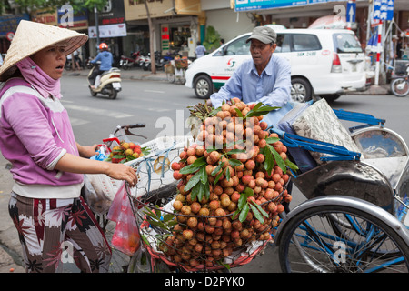 Ein Zyklus-Rikscha-Fahrer stoppt, um Obst zu kaufen, von einer Dame außerhalb Ben Thanh Market, Ho Chi Minh, Vietnam, Indochina Stockfoto